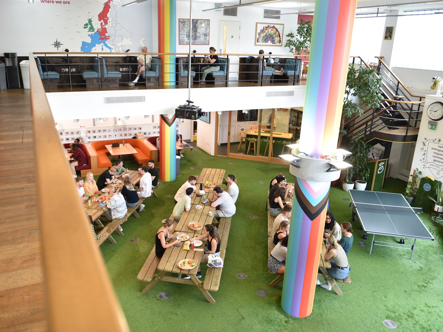 People eating at picnic tables in a modern office with a rainbow pillar.