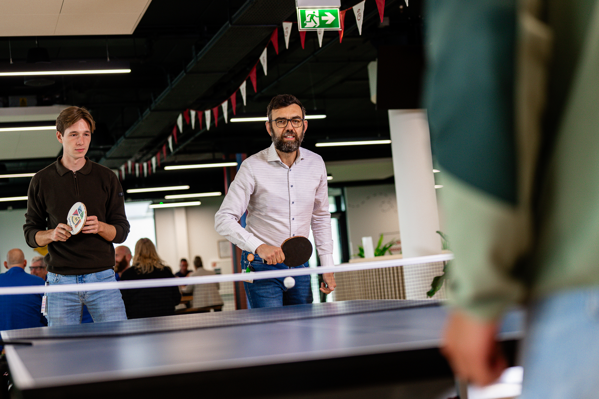 People playing ping pong at the office, with a ball in play.