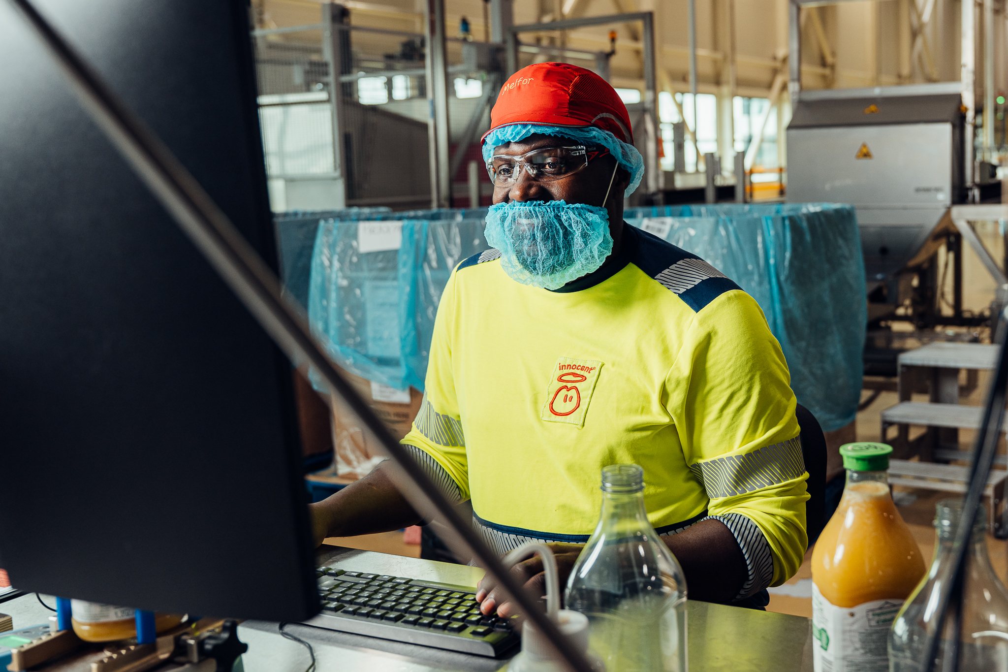 Man wearing protective gear working at a computer in a juice factory.