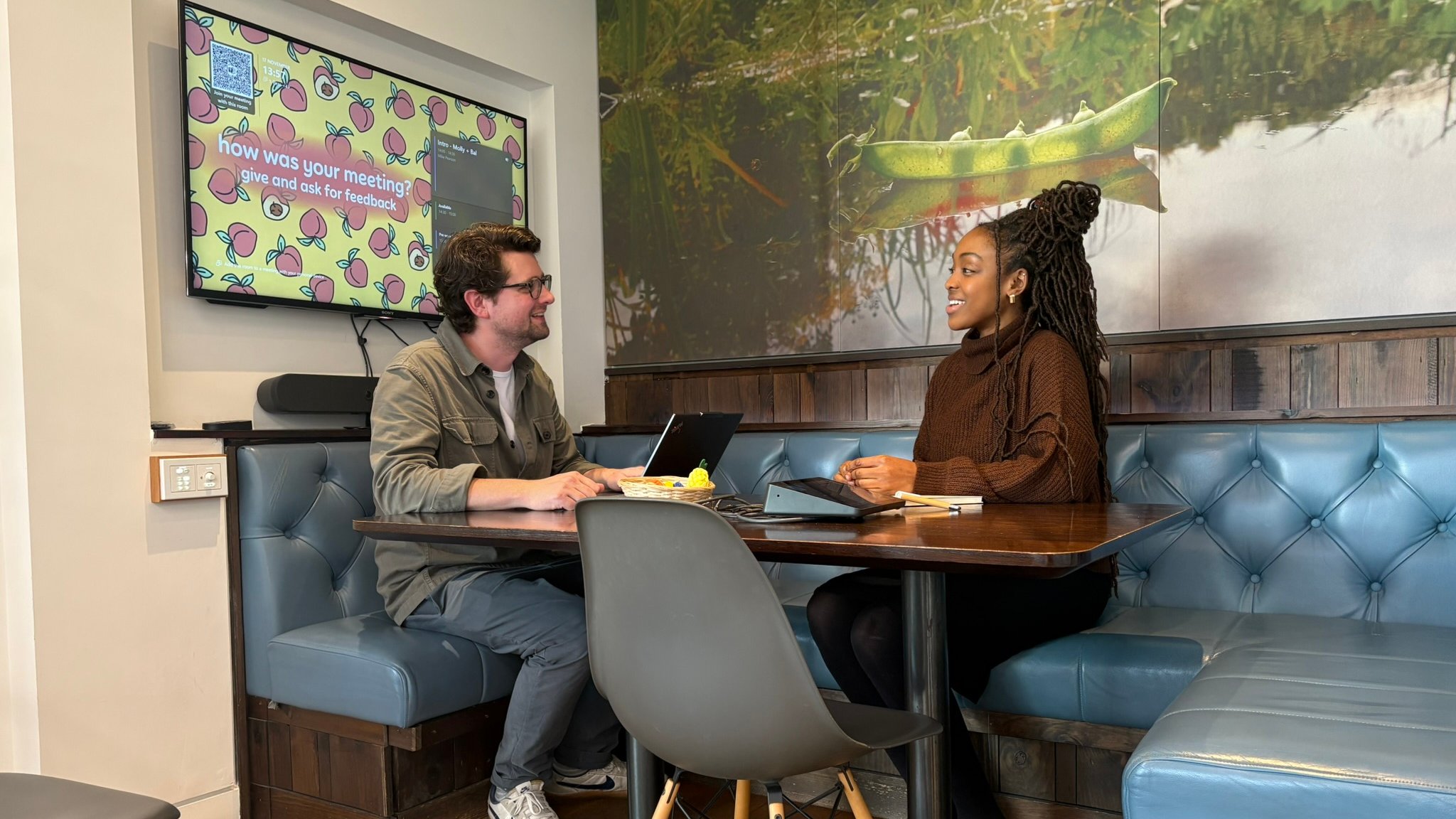 Two people at a table, laptops, screen.